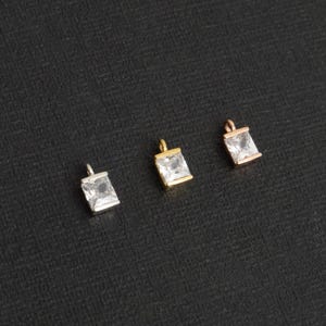May include: Four square-shaped charms with clear rhinestones, each charm has a loop at the top for attaching to jewelry. The charms are in gold, silver, and rose gold.
