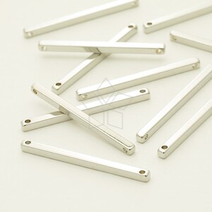 May include: Several shiny, silver-coloured rectangular metal bars with rounded edges. Each bar has a small hole at each end. The bars are scattered across a white surface. The arrangement creates a visually appealing display.