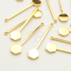 May include: Gold-toned metal hexagon charms with a loop at the top, attached to thin gold-toned metal rods. The charms are scattered on a white surface.