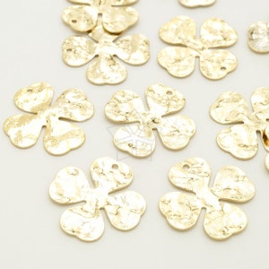 Peut inclure: Un ensemble de breloques en forme de fleur en métal doré avec une texture martelée. Les breloques ont une forme de trèfle à quatre feuilles avec un trou en haut pour les attacher à des bijoux ou d'autres objets artisanaux.