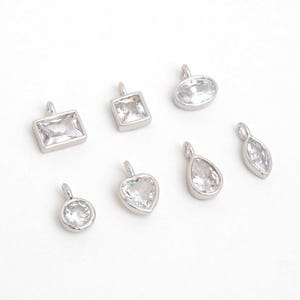 May include: A selection of silver pendants, each set with a clear, sparkling cubic zirconia stone. The pendants come in diverse shapes: rectangular, square, oval, heart, teardrop, and marquise. Each has a small loop for attaching to a chain or bracelet.