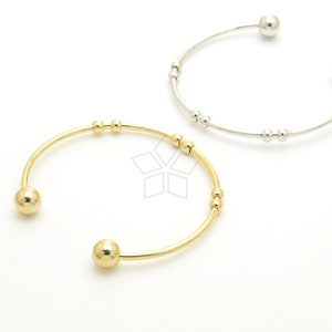 May include: Two bangle bracelets, one gold and one silver, with small round beads. Both bracelets have larger round beads at the ends.