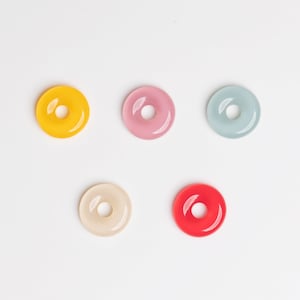May include: Five colorful donut-shaped rings. The rings are in shades of yellow, pink, light blue, cream, and red.