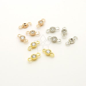 Może przedstawiać: Zestaw małych, ozdobnych łączników do biżuterii z przezroczystymi kryształami w wykończeniach złotym, różowym złotem i srebrnym. Każdy łącznik ma dwie pętle do mocowania do elementów biżuterii.