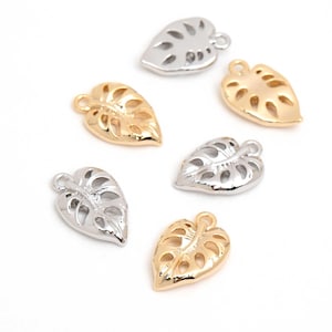 May include: Six metal leaf charms in gold and silver tones. Each charm has a loop for attaching to jewelry and a cut-out design. The charms are arranged on a white background.