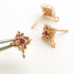 May include: Three gold-tone earring findings with a filigree design and a small red gemstone in the center. Each finding has a loop at the bottom for attaching a dangle.