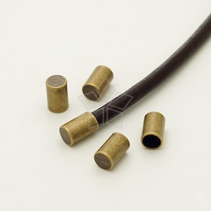 May include: Five antique gold-toned metal cord end caps for leather cord. The cord end caps are cylindrical and have a smooth, slightly textured surface.