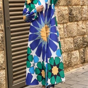 Peut inclure: Une longue robe à manches longues et col, à motifs blancs, bleus, verts et jaunes. La robe est ouverte à l'avant et présente un motif géométrique.