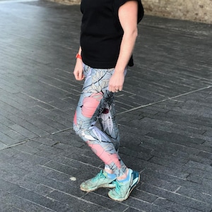 May include: A black short-sleeved shirt paired with leggings featuring a light gray background and a botanical print of large coral-colored flowers and dark gray leaves. The outfit is completed with light blue and white athletic sneakers.