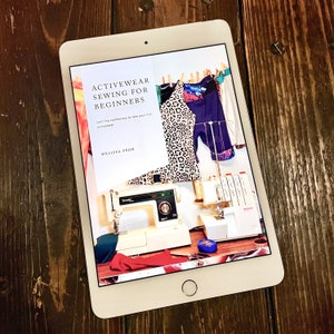 May include: A tablet screen displaying a book cover for "Activewear Sewing for Beginners" by Melissa Fehr. The cover features a leopard print top, a pair of shorts, and a sewing machine.