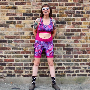 May include: A woman wearing a pink and blue patterned cycling shorts with a matching sports bra. She is wearing white sunglasses and white polka dot socks.