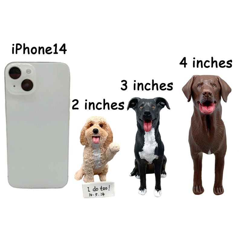 Op de afbeelding: Drie hondenbeeldjes: een 5 cm tan hond, een 7,6 cm zwart-witte hond en een 10 cm bruine hond. De tan hond heeft een poot omhoog en een bordje met de tekst "I do too! 10-5-24". De honden staan naast een iPhone 14.