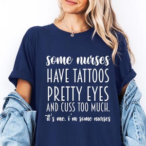 May include: Navy blue t-shirt with white text that reads "some nurses HAVE TATTOOS PRETTY EYES AND CUSS TOO MUCH. It's me. I'm some nurses." A denim jacket is draped over the shoulders. A navy blue circle with the word "Navy" is in the bottom right.