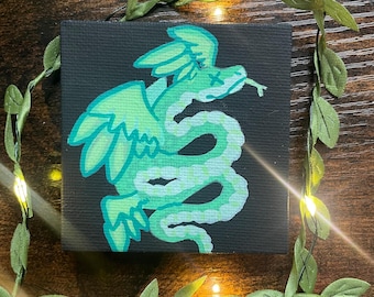 May include: A square canvas artwork depicting a stylized, winged snake in shades of green on a black backdrop. The snake has a forked tongue and an 'X' for an eye. The artwork is framed by a green garland with small lights.