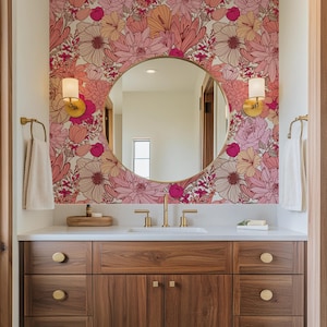 May include: A bathroom vanity with a white countertop and wooden cabinets. The vanity has a round mirror with a gold frame and a floral wallpaper behind it. There are two gold sconces on either side of the mirror.