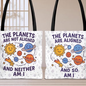 May include: Two white tote bags with black handles. One bag reads "THE PLANETS ARE NOT ALIGNED AND NEITHER AM I" with cartoon planets. The other bag reads "THE PLANETS ARE ALIGNED AND SO AM I" with cartoon planets.
