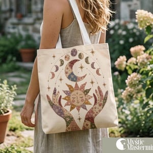 Könnte beinhalten: Eine cremefarbene Stofftasche aus Segeltuch mit weißen Schulterriemen. Die Vorderseite zeigt eine bunte Grafik von zwei Händen, die ein Sonnengesicht halten, umgeben von Mondphasen und Sternen, gefüllt mit floralen und geometrischen Mustern.