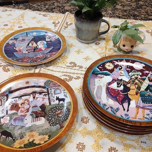 May include: A set of six decorative ceramic plates featuring a nativity scene with a brown, gold, and blue color scheme. The plates are stacked on top of each other and have the years 1981 and 1982 printed on them.