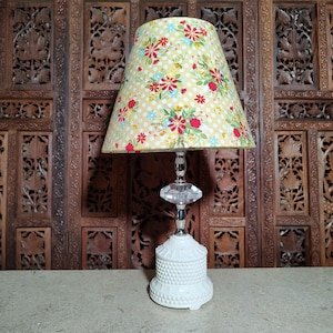 May include: A white ceramic lamp base with a clear crystal finial and a yellow floral lampshade with red and blue accents.