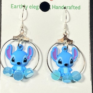 Puede incluir: Un par de pendientes azules del personaje Stitch con aros y ganchos plateados. Los pendientes presentan figuras de Stitch azules y moradas con cuentas facetadas azules. Los pendientes est&aacute;n hechos a mano.