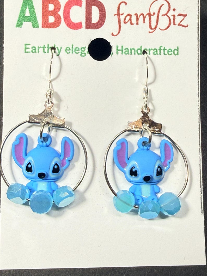 Puede incluir: Un par de pendientes azules del personaje Stitch con aros y ganchos plateados. Los pendientes presentan figuras de Stitch azules y moradas con cuentas facetadas azules. Los pendientes est&aacute;n hechos a mano.