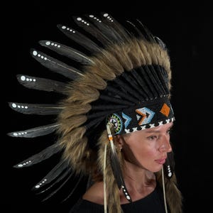 May include: A Native American headdress featuring black and brown feathers with white dot accents. The headdress has a black beaded band with blue, orange, and white geometric patterns. The headdress is trimmed with brown fur.