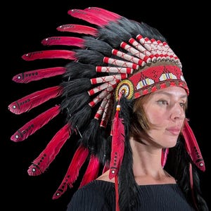 May include: A Native American headdress featuring vibrant red and black feathers. The headdress has a beaded red and white headband with intricate patterns. The feathers are arranged in a fan shape, creating a striking visual display.