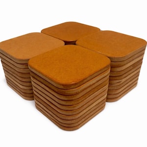 May include: Four stacks of square, light brown coasters with rounded corners. Each stack appears to contain many individual coasters. The coasters are made of a light brown material and are arranged in a square formation.