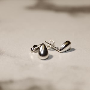 May include: A pair of silver teardrop shaped stud earrings.