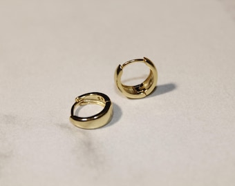 May include: A pair of gold hoop earrings. The earrings are simple and elegant, with a smooth, rounded finish.