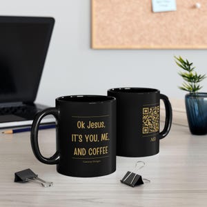 May include: Two black ceramic mugs featuring gold text. One mug displays the phrase "Ok Jesus, IT'S YOU, ME, AND COFFEE" with "Gateway Designs" below. The other mug shows a gold QR code above the Greek letters Alpha and Omega.