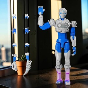 Pode incluir: Uma figura de rob&ocirc; articulada azul, branca e cinza com m&atilde;os intercambi&aacute;veis. O rob&ocirc; tem um design detalhado, com um torso e membros azuis, e detalhes brancos e cinza. M&atilde;os adicionais s&atilde;o exibidas &agrave; esquerda do rob&ocirc;, junto com uma pequena planta em vaso.