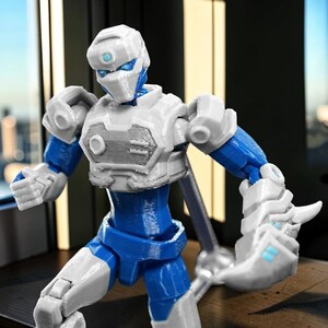 Pode incluir: Figura de a&ccedil;&atilde;o de rob&ocirc; azul e branco com juntas articuladas. A figura tem um capacete e armadura de peito brancos, membros azuis e detalhes mec&acirc;nicos. A figura est&aacute; em uma pose din&acirc;mica, sugerindo a&ccedil;&atilde;o.