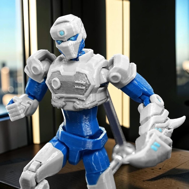 Pode incluir: Figura de a&ccedil;&atilde;o de rob&ocirc; azul e branco com juntas articuladas. A figura tem um capacete e armadura de peito brancos, membros azuis e detalhes mec&acirc;nicos. A figura est&aacute; em uma pose din&acirc;mica, sugerindo a&ccedil;&atilde;o.
