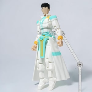 Könnte beinhalten: Eine weiße Actionfigur mit langem Mantel, akzentuiert mit hellblauen und goldenen Details. Die Figur hat schwarzes Haar und wird mit einem transparenten Ständer präsentiert. Das Outfit der Figur hat ein futuristisches Design.