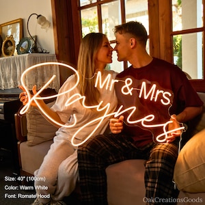 May include: A warm white neon sign that reads "Mr & Mrs Raynes" in a cursive font. The sign is 40 inches (100cm) wide and is held by a couple. The sign is a decorative item.