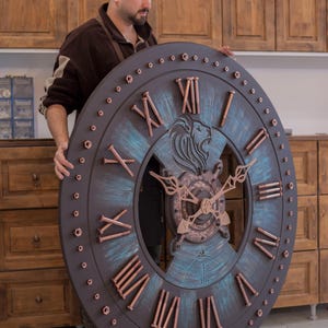 May include: Large, round wall clock with a dark gray frame and copper-colored Roman numerals. The clock face features a lion's head and intricate copper-colored clock hands. The clock is approximately 48 inches in diameter.
