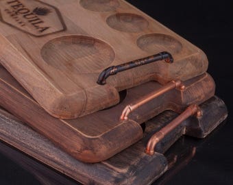 May include: Three wooden serving trays with copper and black metal handles. The top tray has seven round indentations and the text "TEQUILA" engraved on the surface.