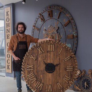 May include: Large, round wooden clock with Roman numerals and a dark brown finish. The clock has a stitched border and a black center. A sign that says "KÖHNE CLOCK" is visible.