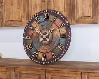 May include: A large, round wall clock with a distressed, multi-colored face. The clock features Roman numerals and the text "Ronne Clock Since 1998". The clock hands are gold-colored, and the clock is displayed on a wooden surface.