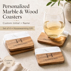 Puede incluir: Juego de cuatro posavasos personalizados de mármol y madera. Cada posavasos tiene una parte superior de mármol blanco y una base de madera, con la inicial "H" y el nombre "HOWARD" grabados. Una copa de vino descansa sobre uno de los posavasos.