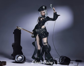 May include: A doll dressed in a black outfit, holding a microphone and a guitar. The doll is wearing a hat and boots. A guitar case and speakers are in the background. The doll is standing in front of a gray background. The text "Shugo Fairy" is visible.