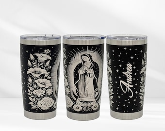 May include: Three black stainless steel tumblers with silver rims and lids. One tumbler features a floral design, another depicts a religious figure, and the third has the name "Andrea" in white script. The tumblers are decorated with white floral and star patterns.