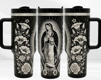 May include: Black travel mug with a handle and a black lid. The mug features a white illustration of the Virgin Mary surrounded by a radiant halo. White floral designs, including roses and other flowers, adorn the mug's surface.