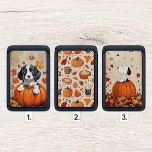 May include: Three phone card holders with fall-themed designs. One features a black and white puppy on a pumpkin, another has pumpkins and fall treats, and the last shows Snoopy on a pumpkin.