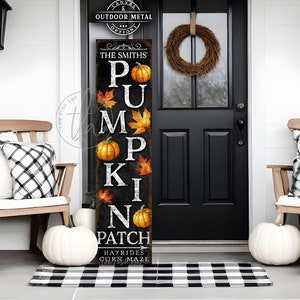 May include: A black and white sign with the words "The Smiths' Pumpkin Patch" and a pumpkin graphic. The sign is hanging on a door with a wreath. There is a black and white chequered rug on the ground.