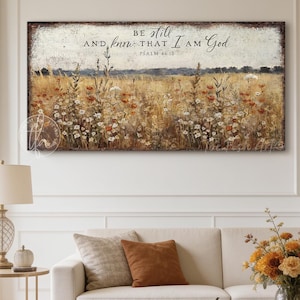 Peut inclure: Une impression murale rectangulaire représentant un paysage de champ de blé doré avec des fleurs sauvages éparpillées sous un ciel nuageux. Le texte "BE still AND know THAT I AM God PSALM 46:10" est imprimé en noir au centre supérieur.