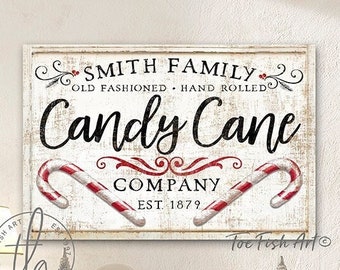 Puede incluir: Un cartel blanco con texto negro que dice "Smith Family Old Fashioned Hand Rolled Candy Cane Company Est. 1879". El cartel está decorado con bastones de caramelo rojos y blancos. El cartel está colgado en una pared blanca con una mesa de madera y decoraciones navideñas delante.