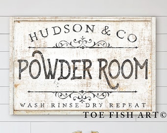 May include: A white sign with black text that reads "Hudson & Co. Powder Room Wash. Rinse. Dry. Repeat Toe Fish Art." The sign is hanging on a white shiplap wall above a white clawfoot bathtub with gold fixtures.