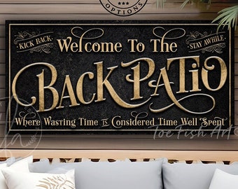 Pode incluir: Um banco de jardim de madeira com almofadas brancas e almofadas cinzentas. Acima do banco, há uma placa preta com letras douradas que diz "Welcome To The Back Patio". A placa também inclui o texto "Kick Back" e "Stay Awhile".